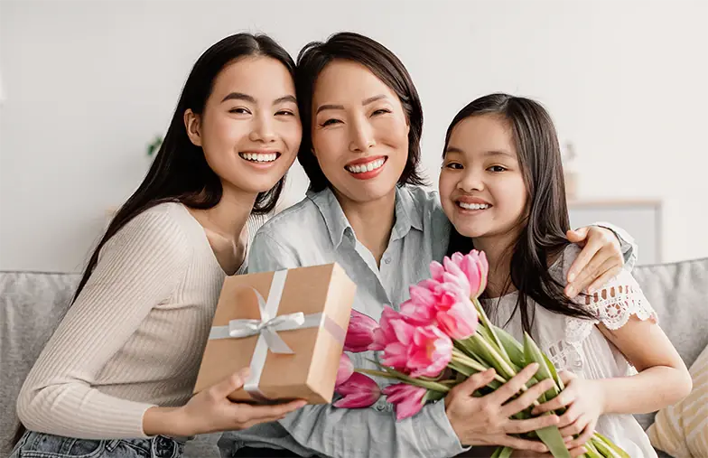 A mum laughing as her two daughters give her a wrapped gift and flowers