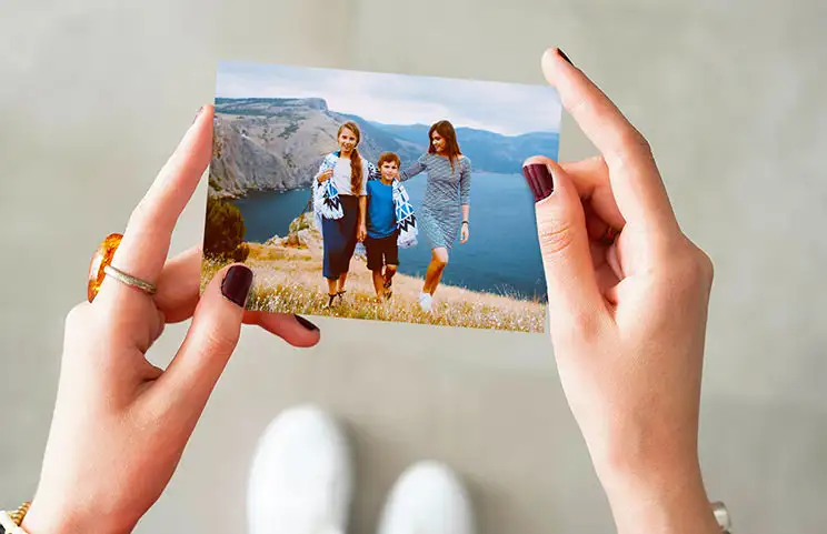 Hands holding a photo print of three kids on holiday